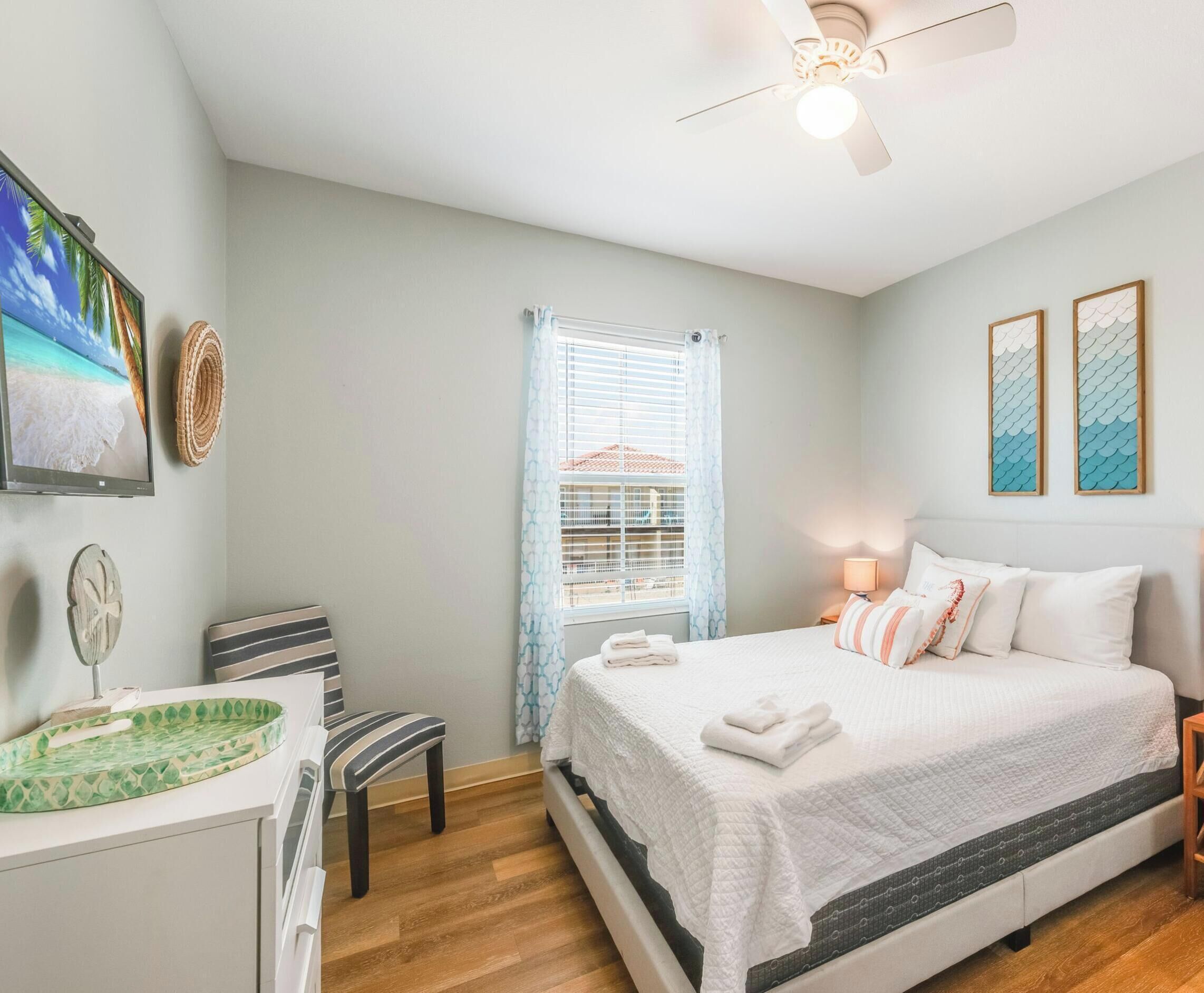 A bedroom with a bed, a desk, a chair, a ceiling fan, and a window with blinds.