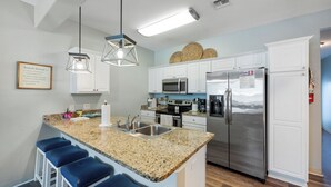 A modern kitchen with granite countertops, stainless steel appliances, and bar stools. - Dog-Friendly Townhome | Heated Pool & Short Walk to Beach (Corpus Christi)