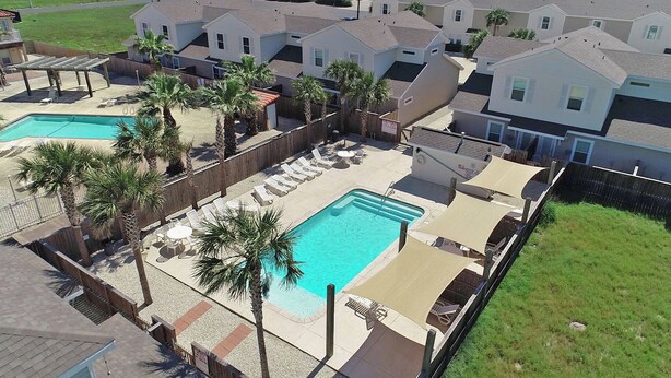 A residential area with a swimming pool, lounge chairs, and palm trees. - Dog-Friendly Townhome | Heated Pool & Short Walk to Beach (Corpus Christi)