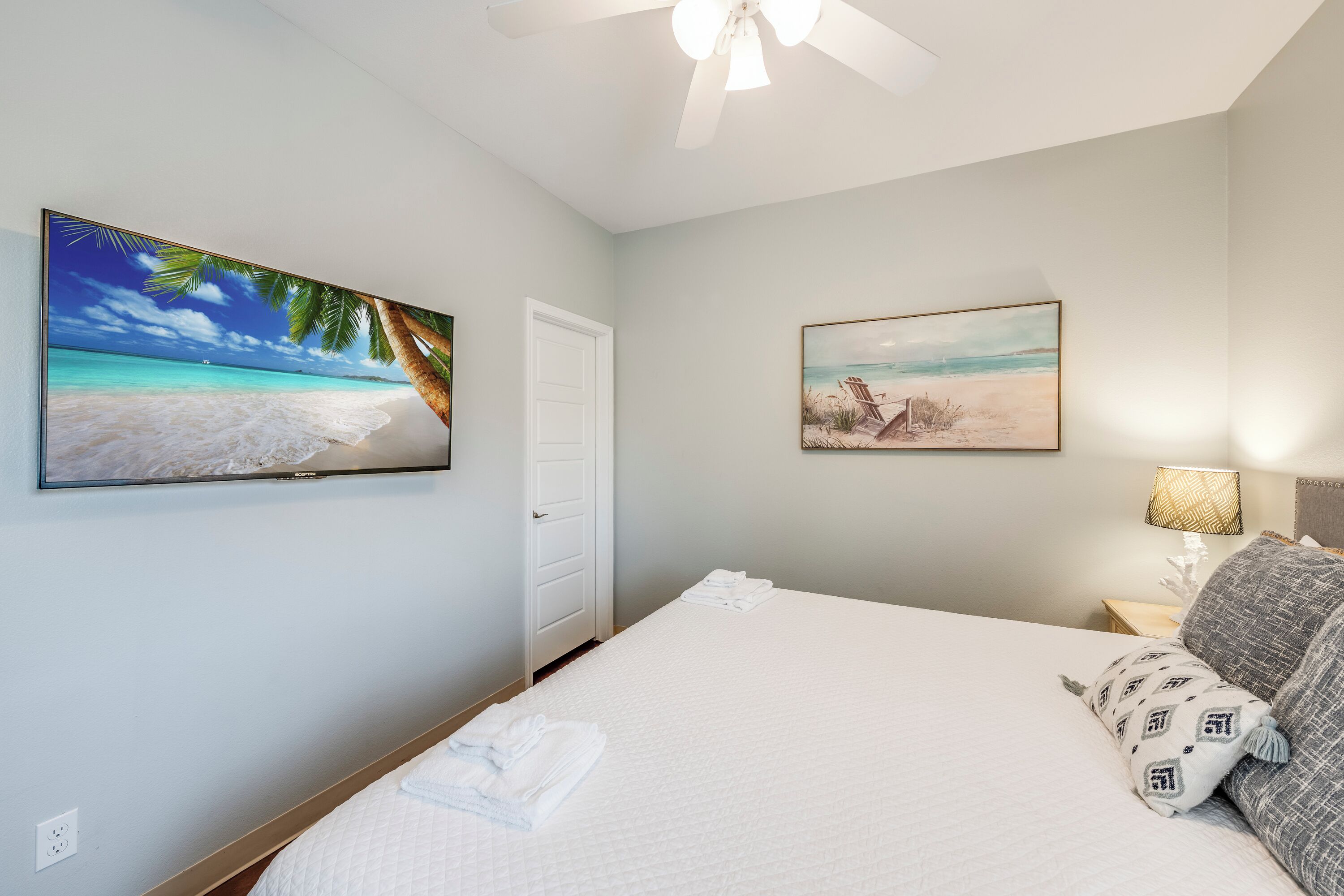 A bedroom with a bed, a ceiling fan, a door, and two wall-mounted paintings.