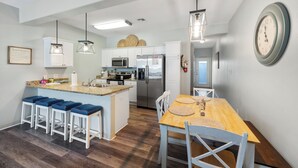 A modern kitchen with white cabinets, a stainless steel refrigerator, and a wooden dining table with bar stools. - Dog-Friendly Townhome | Heated Pool & Short Walk to Beach (Corpus Christi)