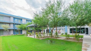 A courtyard with a covered seating area, a small pond, and a building with blue and white exterior walls. - Sleek Stay 4mins to State Farm Stadium (Glendale)