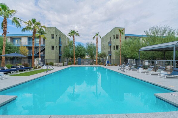 A swimming pool with lounge chairs and palm trees, surrounded by buildings with balconies. - Sleek Stay 4mins to State Farm Stadium (Glendale)