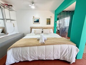 A neatly made bed with a white and beige duvet, a ceiling fan, and a framed picture on the wall. - Cozy 1-bedroom studio in charming Arecibo with AC , JACUZZI and a KING BED (Arecibo)