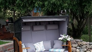 Een houten buitenbank met kussens en een kleine tafel, geplaatst tegen een stenen muur en omringd door groen.