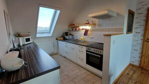 Een kleine keuken met een raam, een magnetron, een spoelbak en een fornuis.
