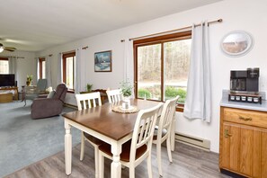 A dining area with a wooden table, white chairs, a television, and a coffee maker. - Bradford County Creekside Country Retreat (Millerton)