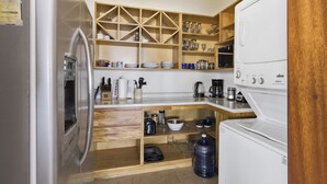 A compact kitchen with wooden shelves, a refrigerator, a coffee maker, and a water dispenser. - Two Bedroom Penthouse Palapa Ocean View (Puerto Escondido)