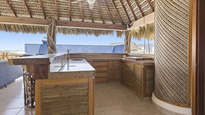 A kitchen with a curved island, wooden cabinets, and a thatched roof. - Two Bedroom Penthouse Palapa Ocean View (Puerto Escondido)