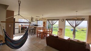 A spacious living area with a hammock, a dining table with chairs, a sofa, and large windows offering a view of the outdoors. - House with sea view, a few steps from the magnificent Gouérou beach. (Lampaul-Plouarzel)
