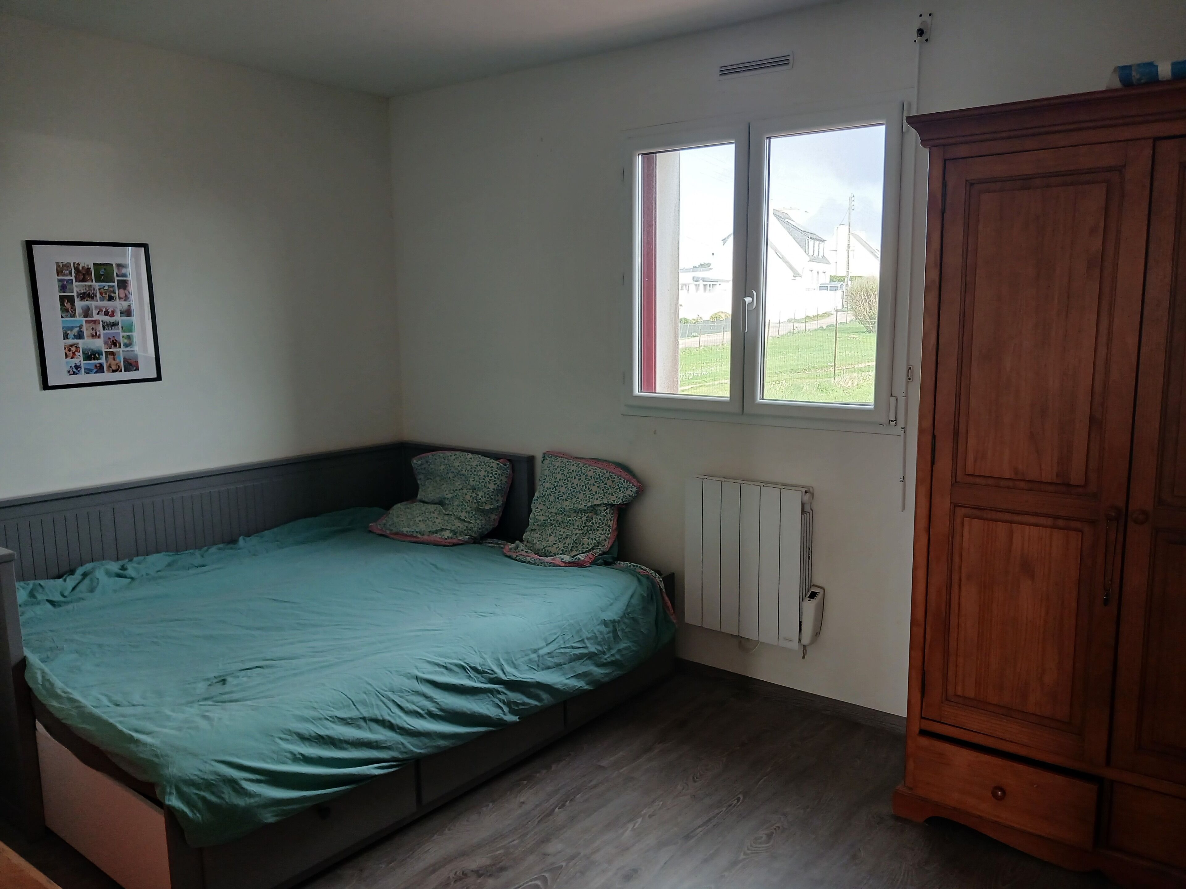 Un dormitorio con cama, un radiador, una ventana y un armario de madera.