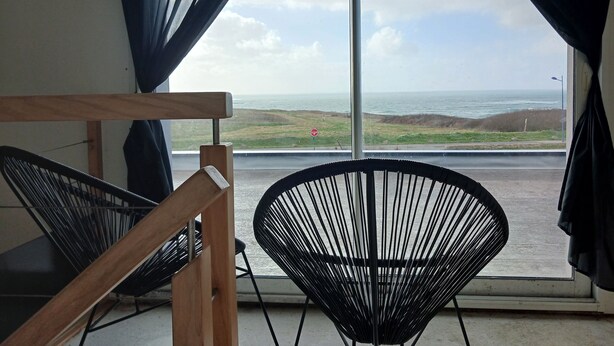 A room with a view of the sea, a wooden chair, a black chair, and a window with curtains. - House with sea view, a few steps from the magnificent Gouérou beach. (Lampaul-Plouarzel)