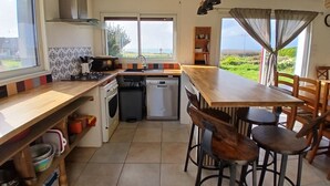 A kitchen with a wooden countertop, a dishwasher, a stove, and a sink. There are chairs around a wooden table. - House with sea view, a few steps from the magnificent Gouérou beach. (Lampaul-Plouarzel)