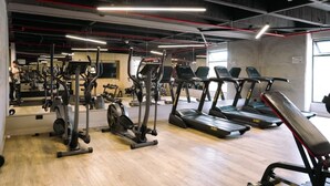 Un gimnasio con diferentes máquinas de ejercicio, una banca y un espejo grande.