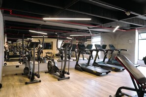 Ein Fitnessraum mit verschiedenen Trainingsgeräten, einer Bank und einer Spiegelwand.