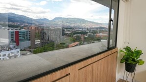 Una habitación con un amplio ventanal que da a una vista panorámica de la ciudad, con edificios y montañas.