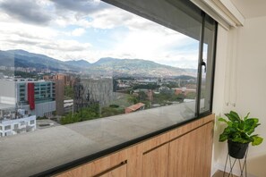 Ein Zimmer mit großem Fenster und Blick auf eine Stadtlandschaft mit Gebäuden und Bergen.