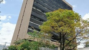 Un edificio moderno con techo plano, ventanas amplias y un área verde circundante con árboles.