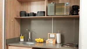 Una cocina compacta con microondas integrado, un refrigerador pequeño y un lavamanos.