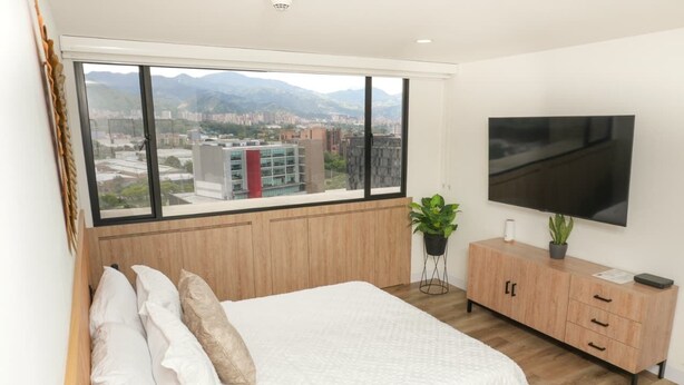 Un dormitorio con un ventanal grande, una cama, un televisor y un armario de madera.