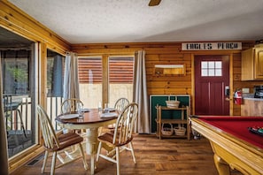 Ein Interieur einer Holzhütte mit Esstisch, Stühlen, einem Billardtisch und einem Schild mit der Aufschrift 'EAGLES PERCH'.