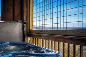 Ein Whirlpool mit einer Holzterrasse und Blick auf Berge durch ein fensterartiges Gitter.