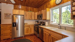A kitchen with wooden cabinets, stainless steel appliances, a sink, and a window with a view. - Cayuga Belle: Gorgeous Cayuga Lake Estate! Fabulous Views! (Seneca Falls)