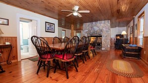 A dining area with a wooden table and chairs, a stone fireplace, and a ceiling fan. - Cayuga Belle: Gorgeous Cayuga Lake Estate! Fabulous Views! (Seneca Falls)