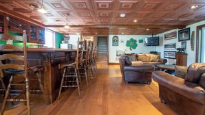 A spacious room with wooden flooring, a bar area with stools, a sofa, and a television mounted on the wall. - Cayuga Belle: Gorgeous Cayuga Lake Estate! Fabulous Views! (Seneca Falls)