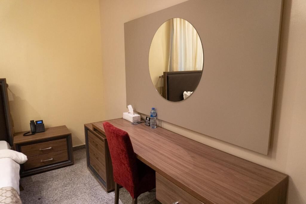 Quarto de hotel com uma escrivaninha de madeira, espelho, telefone, garrafa de água e toalha vermelha.