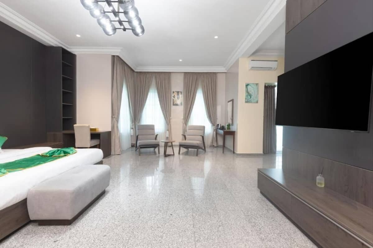 Una habitación de hotel con una cama, dos sillones, un televisor y un amplio armario de madera.