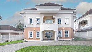 A multi-story residential building with a central balcony, multiple windows, and a paved driveway.
