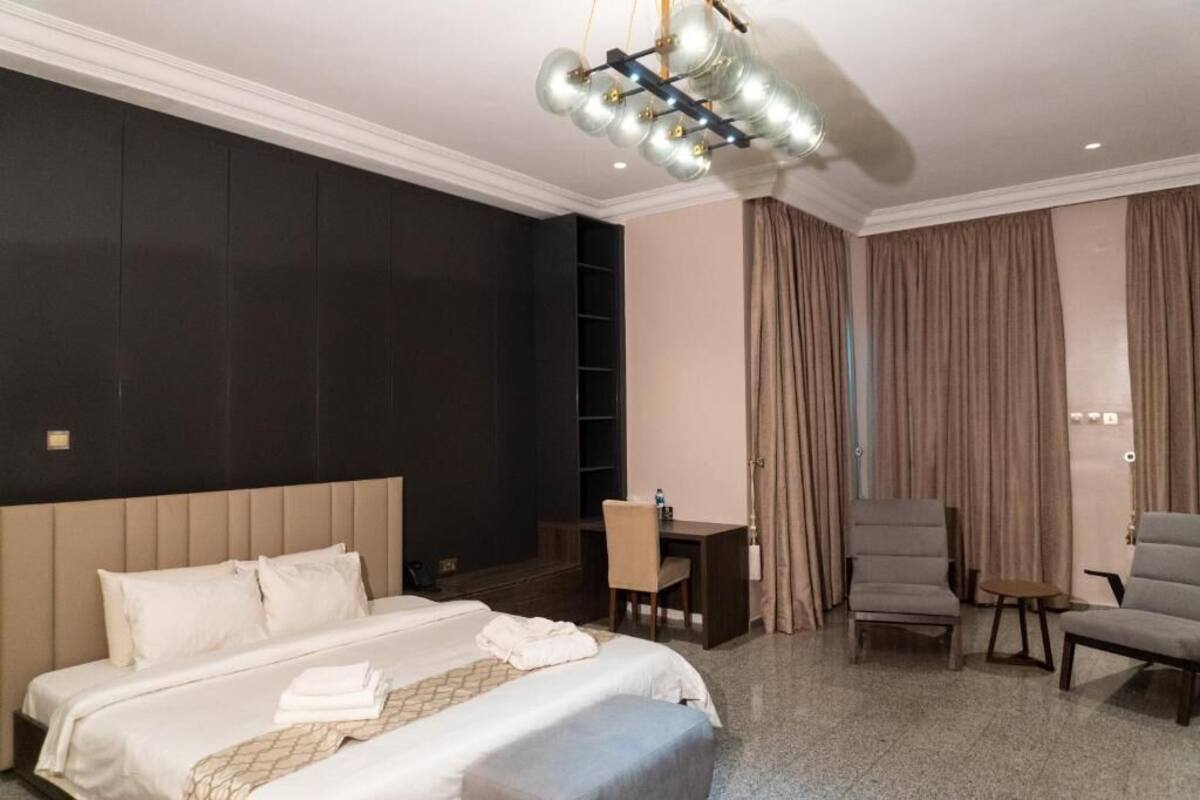 Habitación de hotel con una cama grande, un escritorio, dos sillas, un armario y una araña.