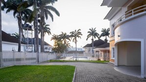 A residential area with a paved driveway, a white fence, and palm trees.