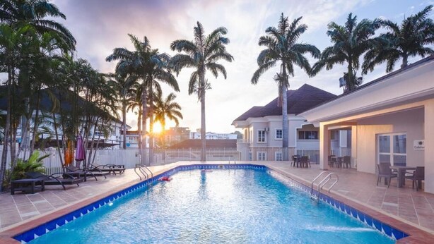 A swimming pool with lounge chairs and palm trees, surrounded by a building with a cafe.
