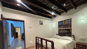 A bedroom with a bed, a bookshelf, a door leading to another room, and a ceiling with exposed beams. - Wonderful 4-bedroom cottage in Kalpetta for a relaxing getaway (Kalpetta)
