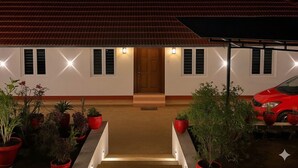 A building with a red-tiled roof, a wooden door, and a red car parked in front. - Wonderful 4-bedroom cottage in Kalpetta for a relaxing getaway (Kalpetta)