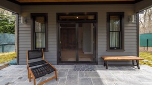 A covered patio with a bench, a chair, and a door leading to an interior space.
