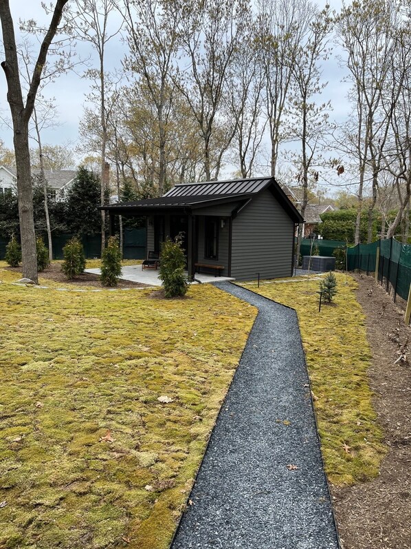 A house with a gravel driveway, a small porch, and a yard with grass and trees. - Lovely studio with AC in charming Sag Harbor (Sag Harbor)