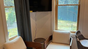 A room with two chairs, a small table, a TV, and large windows with blinds.