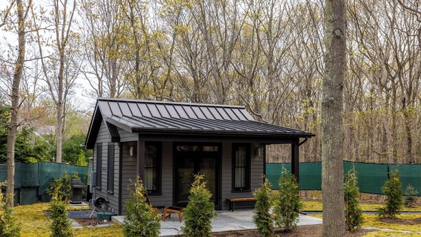 A small cabin with a porch, surrounded by trees and a fenced area.
