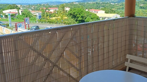 A balcony with a view of a town and mountains, a white table, and a metal railing. - Grand studio lumineux pour 2 ou 4 personnes (Ducos)