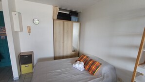 A single bed with a white mattress, a small bedside table, a wardrobe, and a mirror. - Grand studio lumineux pour 2 ou 4 personnes (Ducos)