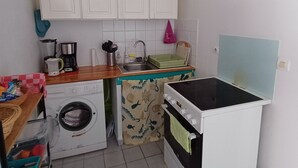 A compact kitchen with a washing machine, a stove, a sink, and white cabinets. - Grand studio lumineux pour 2 ou 4 personnes (Ducos)