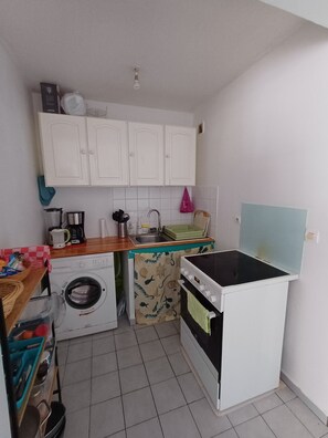 Eine kleine Küche mit Waschmaschine, Herd, Spüle und weißen Schränken.