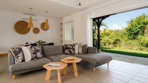 Una sala de estar moderna con un sofá seccional gris, dos mesitas de madera y un comedor con mesa y sillas.