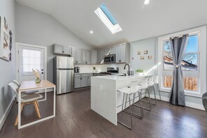 Una cocina moderna con una isla central, armarios blancos, electrodomésticos de acero inoxidable y un tragaluz.