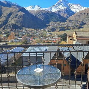 Vista sulle montagne con una valle e un paese, un tavolo con un cuscino, e un edificio con tetto spiovente.