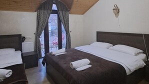 A bedroom with two beds, a window with curtains, a ceiling light, and a wall-mounted lamp. - OTEL IVERIA (Stepantsminda)