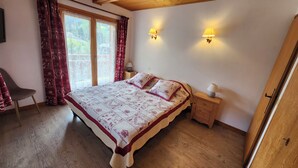 Um quarto com uma cama, uma cadeira, uma mesa de cabeceira, uma luminária e uma janela com cortinas.